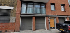 A two-story building with a garage door, a wooden door, and a vehicle parked in front. - Modern 2 BDR Balcony near Oxford Street (London)