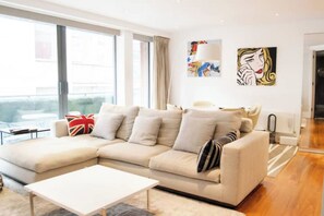 A modern living room with a beige sectional sofa, a white coffee table, and artwork on the walls. - Modern 2 BDR Balcony near Oxford Street (London)