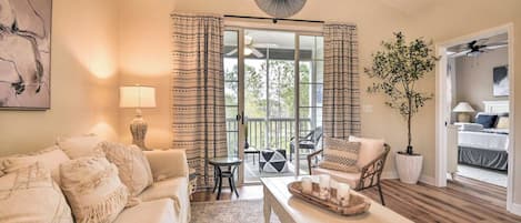 A living room with a sofa, a coffee table, a fan, and a view of the outdoors through a glass door.