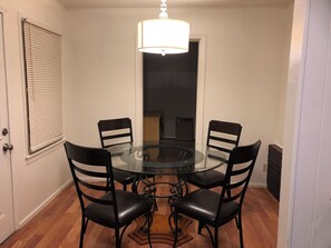 A dining area with a round glass table surrounded by four chairs, a chandelier, and a door with blinds. - Charming 3-bedroom house in adorable Brownsville with AC (Brownsville)