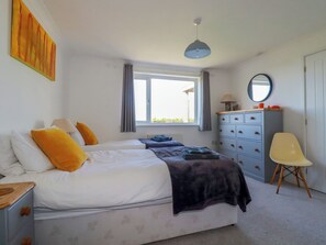 A bedroom with two beds, a dresser, a chair, and a window with curtains. - Mermaid Gaze (Newquay)