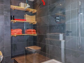 A modern bathroom with a glass-enclosed shower, a toilet, and shelves with towels. - Mermaid Gaze (Newquay)