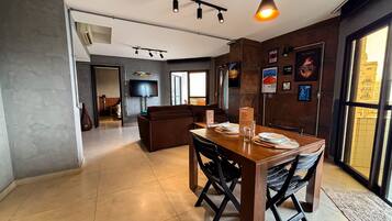Un comedor moderno con una mesa y sillas de madera, un televisor montado en la pared y un gran ventanal que proporciona luz natural.