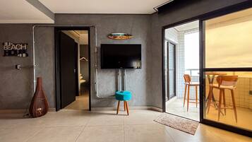 A modern living room with a flat-screen TV mounted on the wall, a small blue ottoman, and a decorative wall piece.
