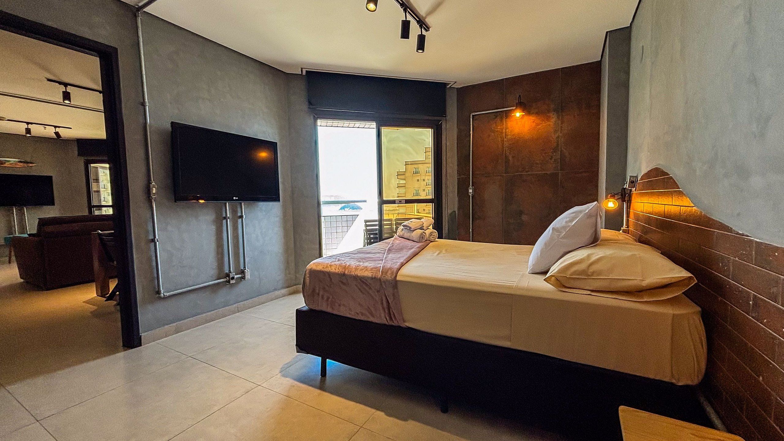 Habitación de hotel moderna con cama, televisión de pantalla plana en la pared y vista a la ciudad desde la ventana.