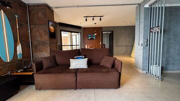 A modern living room with a brown sofa, a wall-mounted TV, and a large window.