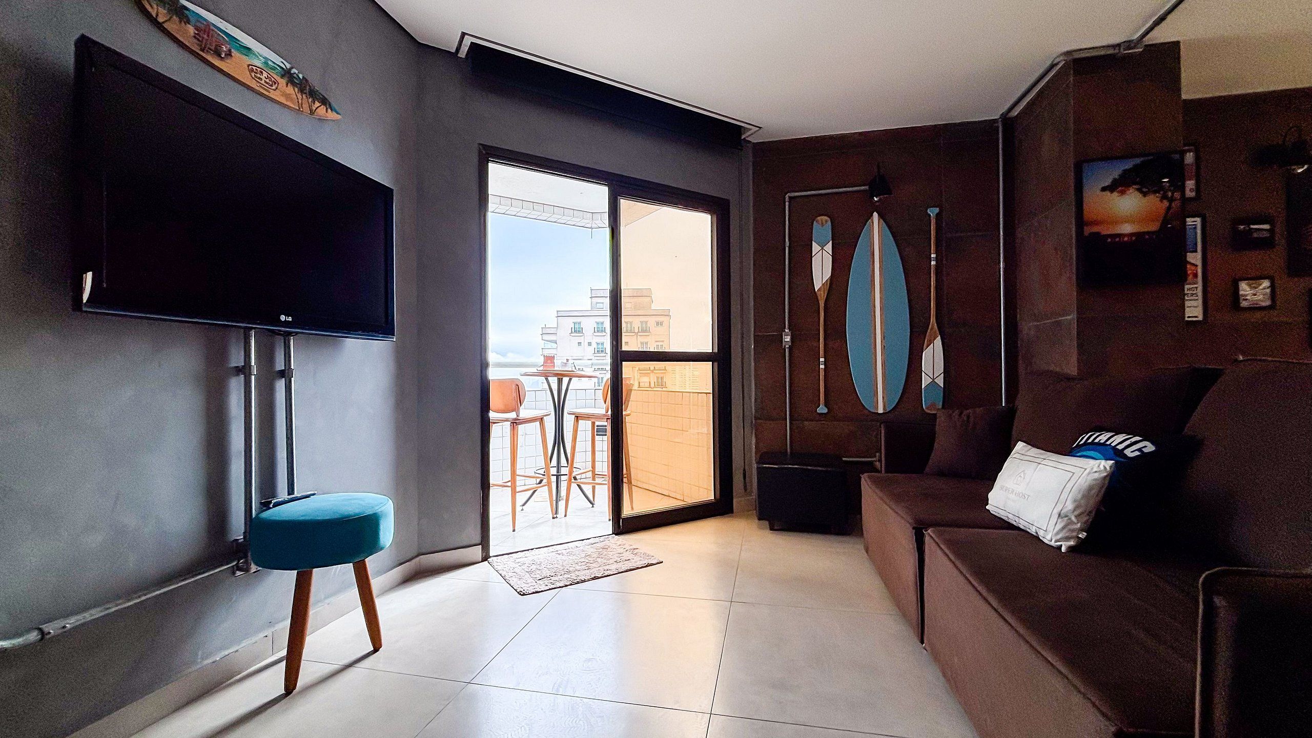 A modern living room with a flat-screen TV, a sofa, a coffee table, and a view of the city through a glass door.