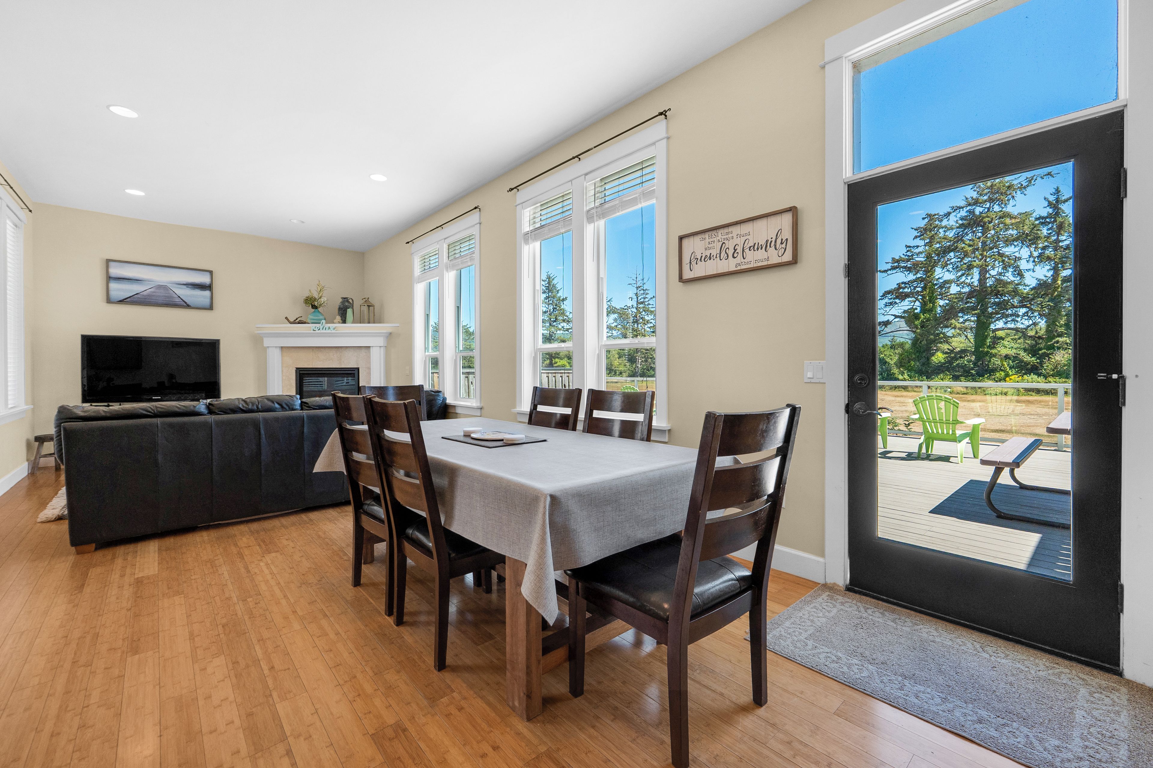 Un coin repas avec une table dressée pour six personnes, flanqué de deux fenêtres équipées de stores, d’une cheminée et d’un téléviseur en arrière-plan.