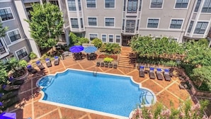 A rooftop swimming pool with lounge chairs and umbrellas, surrounded by greenery and a multi-story building. - King Suite In Charlotte  (Charlotte)