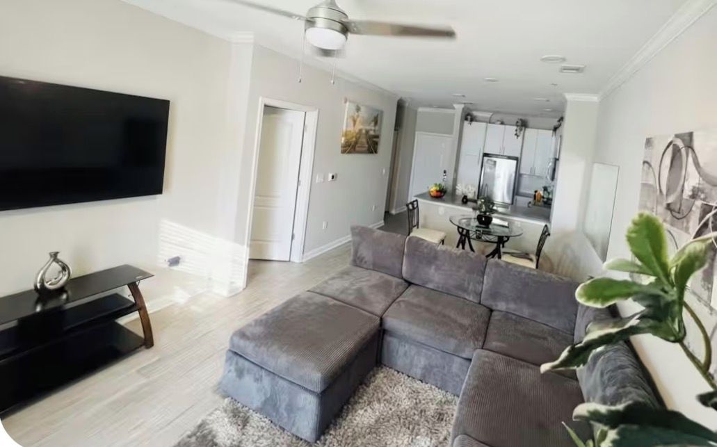 A modern living room with a sectional sofa, a flat-screen TV, and a ceiling fan.