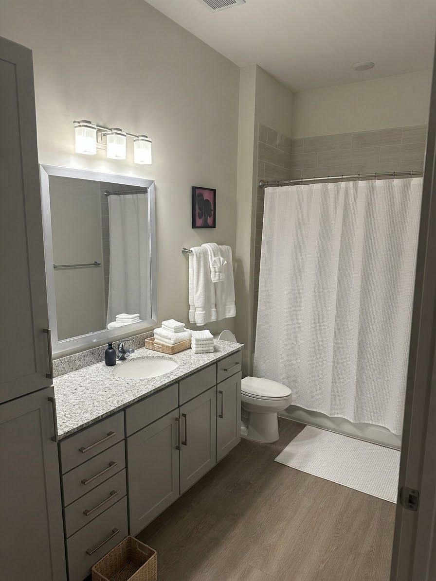 A bathroom with a large mirror, a sink, a toilet, and a shower area.