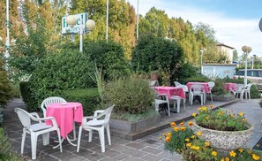 An outdoor seating area with tables and chairs, surrounded by greenery and a sign indicating a hotel.
