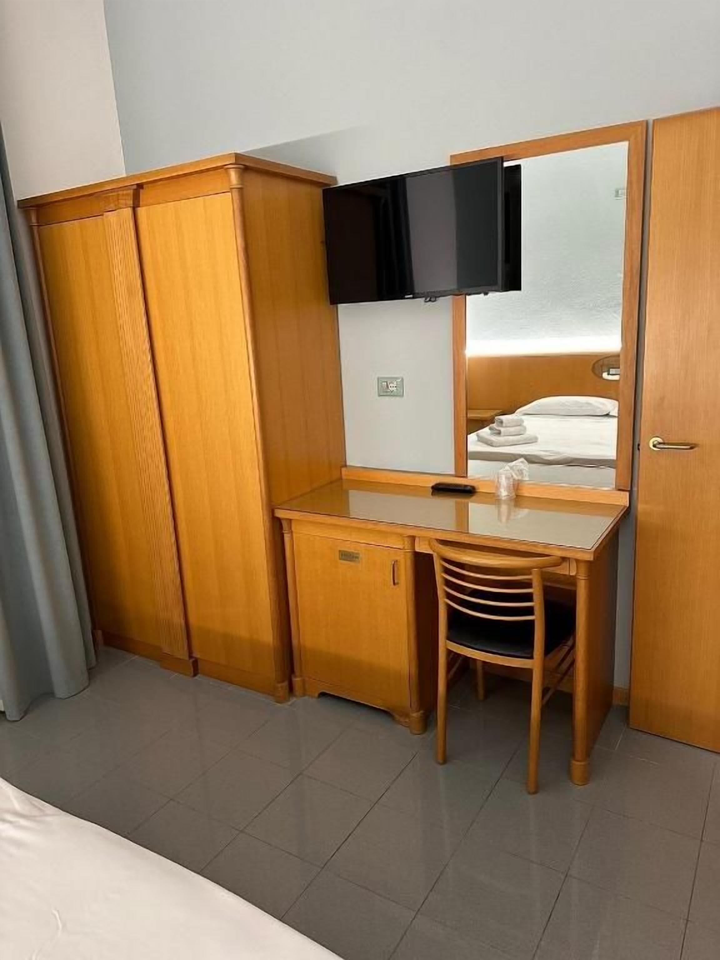 Une chambre d’hôtel avec un bureau en bois, une chaise, un téléviseur fixé au mur et une armoire.