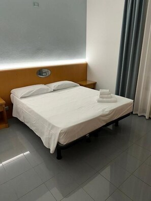 A hotel room with a bed, a nightstand, a wall-mounted clock, and a curtain.