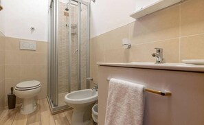 A bathroom with a toilet, bidet, and a glass-enclosed shower. - Hotel Garden (Bologna)