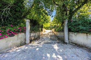 A paved pathway leading through a gated entrance with a stone wall on one side and a metal gate on the other. - La Guate - Maison avec piscine - Saint-Émilion (Daubèze)