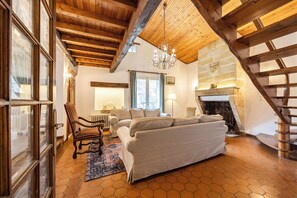 A cozy living room with a sofa, a chair, a fireplace, and a wooden ceiling. - La Guate - Maison avec piscine - Saint-Émilion (Daubèze)