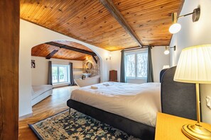 A bedroom with a large bed, a wooden ceiling, a window, and a bathroom visible in the background. - La Guate - Maison avec piscine - Saint-Émilion (Daubèze)