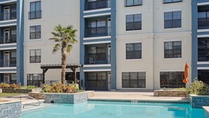 Une piscine dont le bord est revêtu de carrelage, entourée d’un bâtiment doté de nombreux balcons et fenêtres.