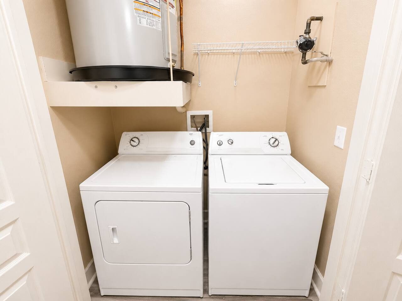 A laundry room with two white washers and dryers, a shelf above the dryers, and a water heater mounted on the wall.