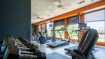 Une salle de sport équipée de matériel d’exercice, notamment des haltères et des tapis de course, et dotée de grandes fenêtres laissant entrer la lumière naturelle.