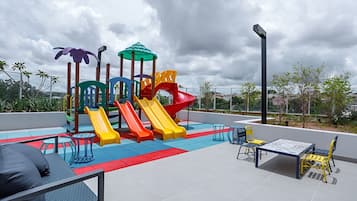 An outdoor play area with slides and climbing structures, surrounded by seating and a table.
