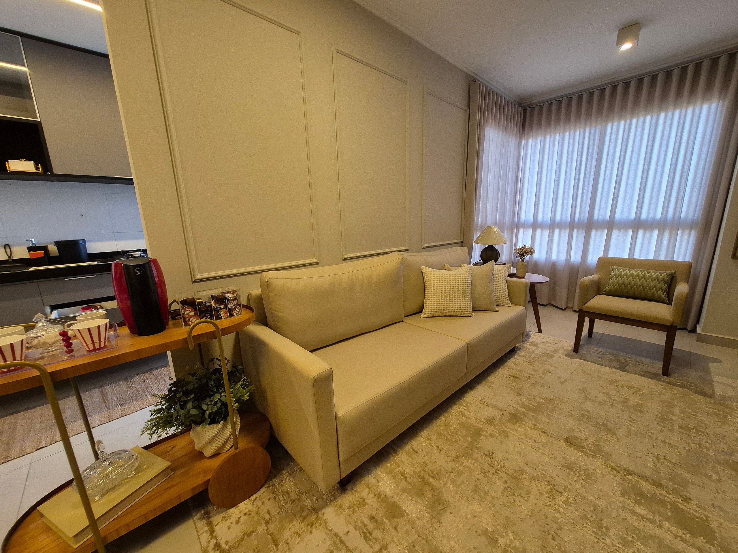 Un salon comprenant un canapé, des fauteuils, une table basse, une lampe, et un coin cuisine à l’arrière-plan.