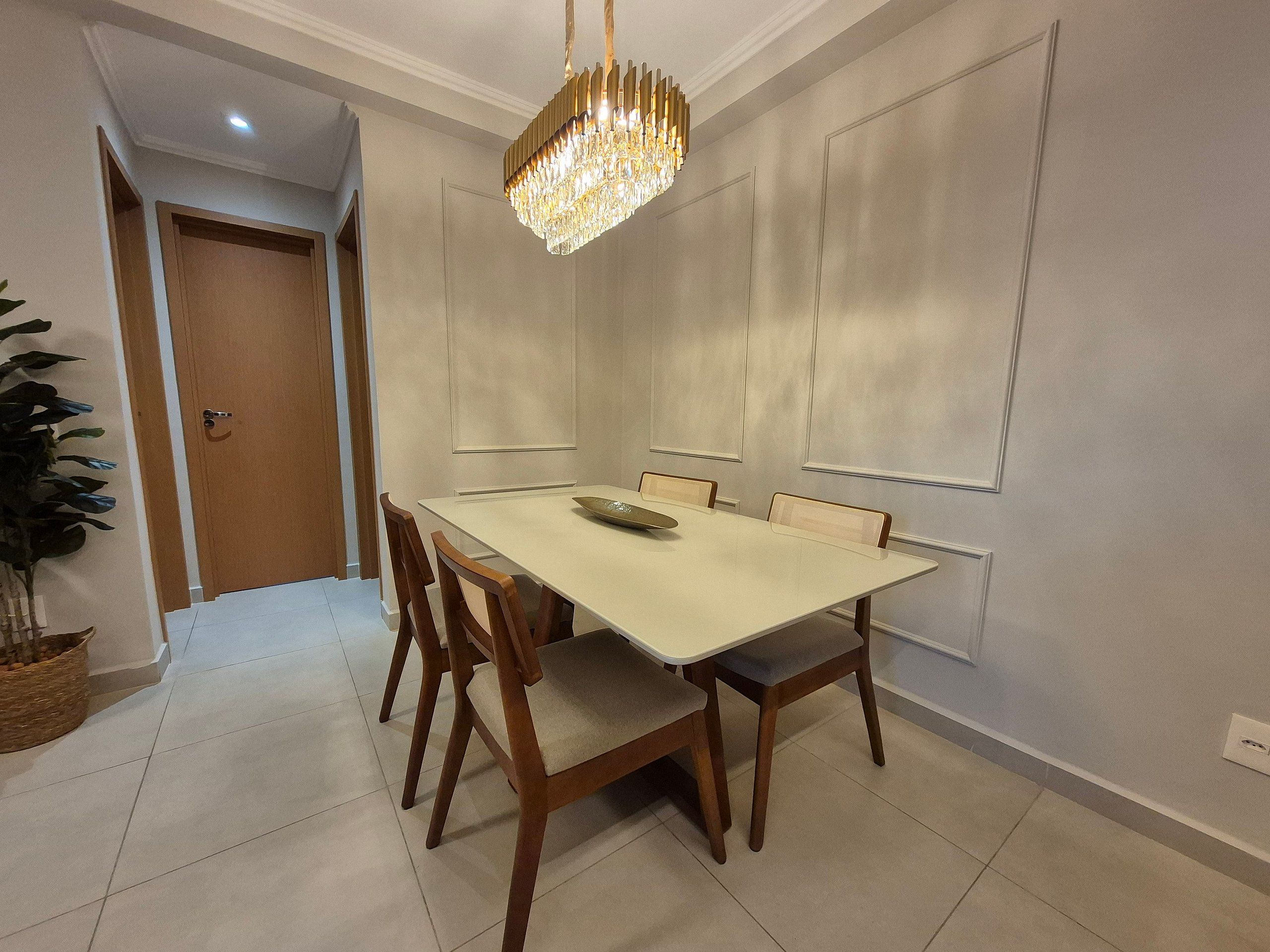 Un comedor con una mesa blanca, sillas de madera, una lámpara de araña y una puerta al fondo.