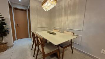 Un comedor con una mesa blanca, sillas de madera, una lámpara de araña y una puerta al fondo.
