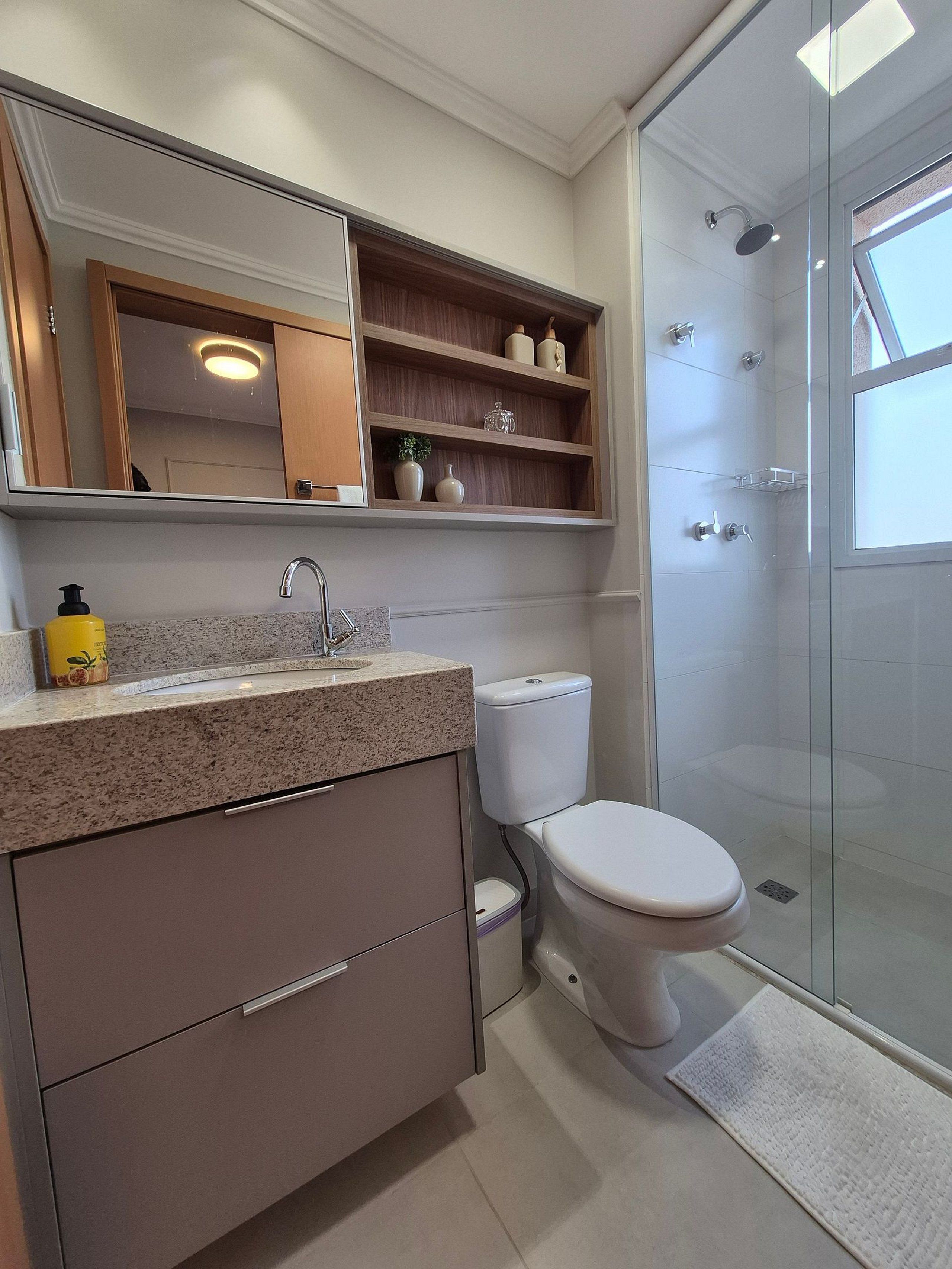 A modern bathroom with a glass shower enclosure, a white toilet, a granite countertop, and a mirror above the sink.