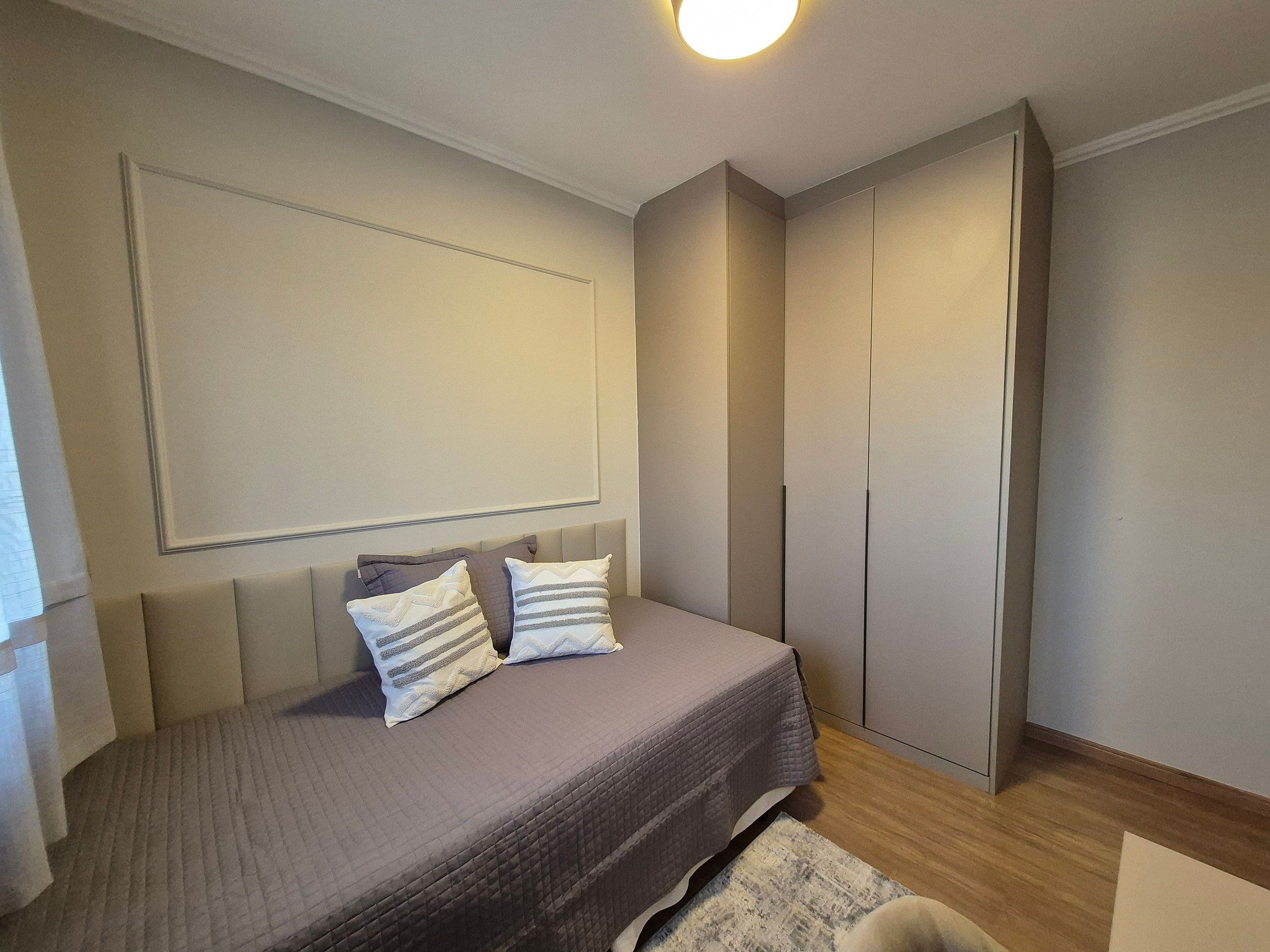 A bedroom with a bed, a wardrobe, and a wall-mounted light fixture.