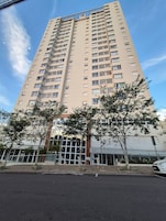 Um edifício alto com vários andares, varandas e céu claro.