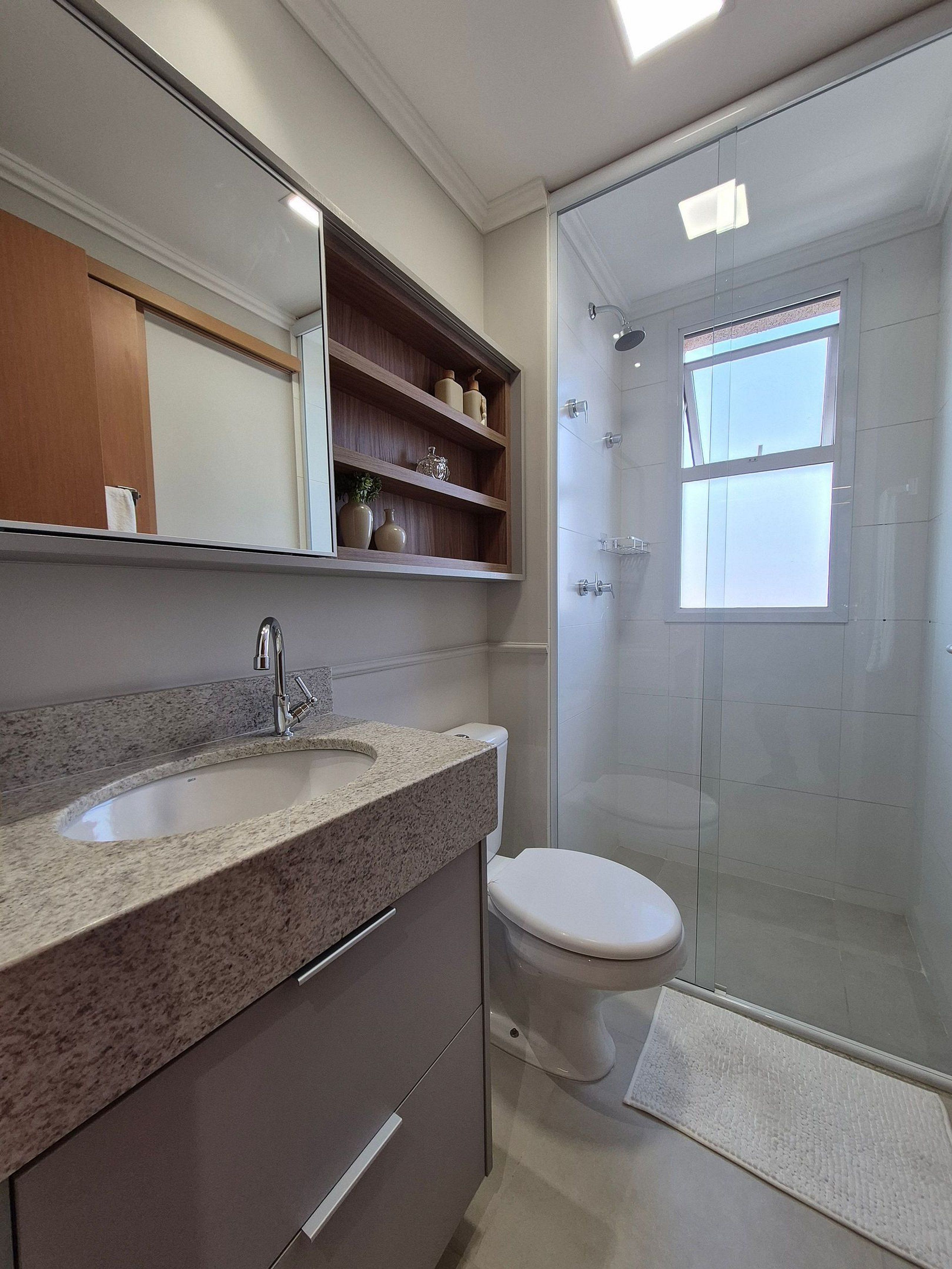 A bathroom with a granite countertop sink, a toilet, a glass shower enclosure, and a mirror above the sink.