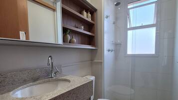 A bathroom with a granite countertop sink, a toilet, a glass shower enclosure, and a mirror above the sink.