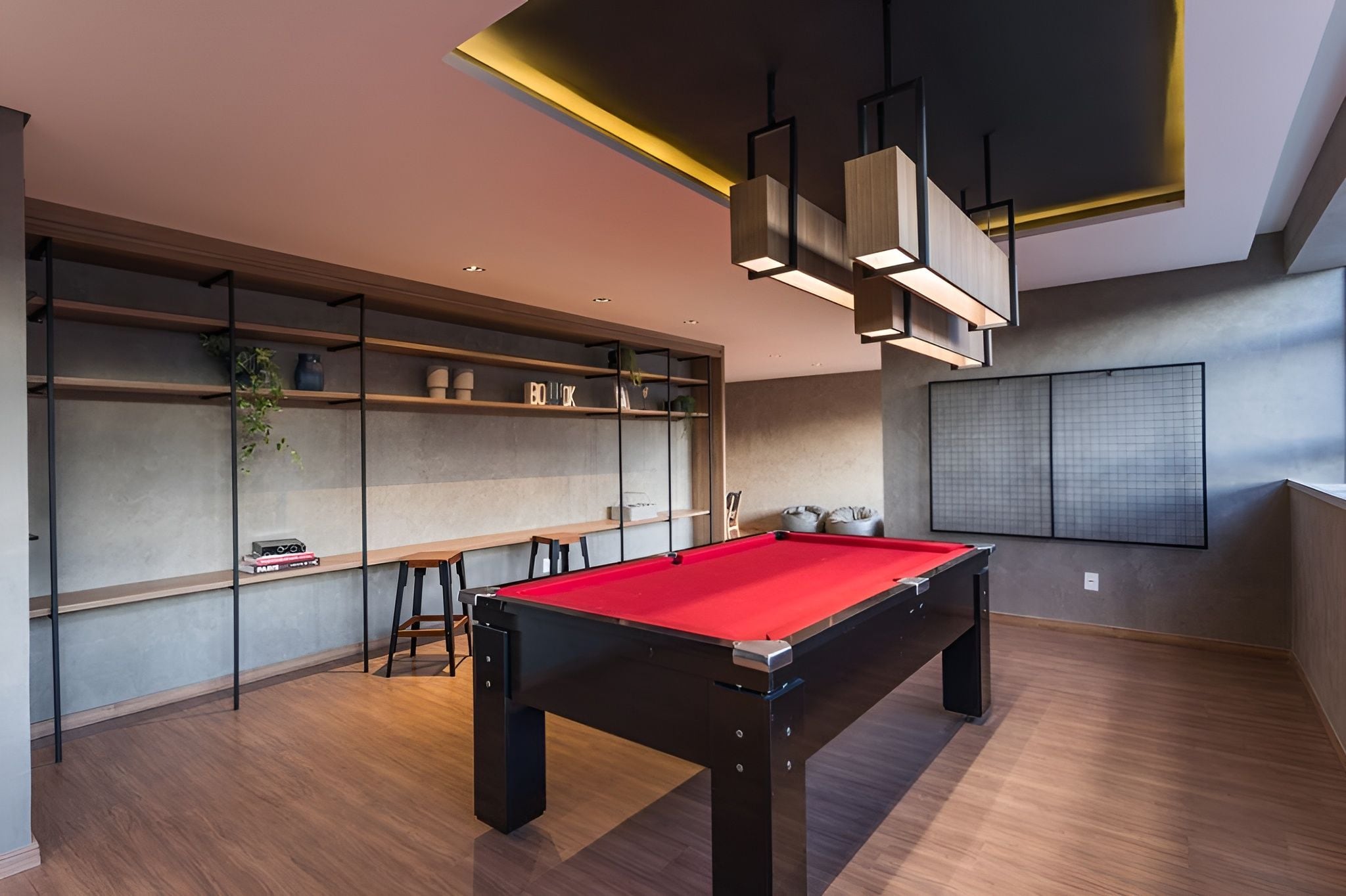 Une table de billard moderne, conçue pour l’intérieur, recouverte d’un drap de feutre rouge, entourée d’un plancher en bois et de rayonnages où sont disposés divers objets.