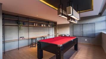 Une table de billard moderne, conçue pour l’intérieur, recouverte d’un drap de feutre rouge, entourée d’un plancher en bois et de rayonnages où sont disposés divers objets.