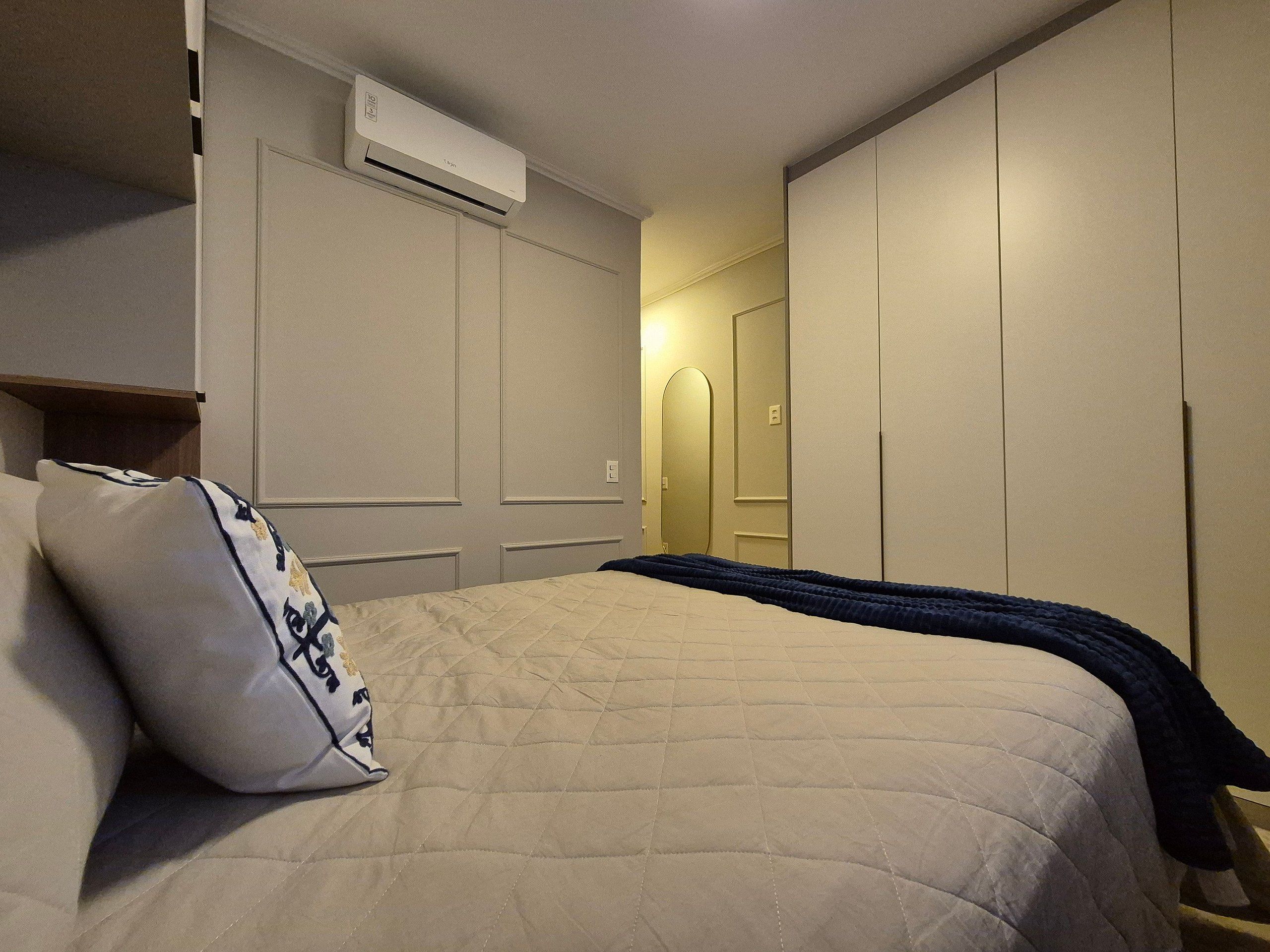 A bedroom with a bed, a pillow, an air conditioning unit, and a wardrobe.