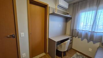 A room with a wooden door, a desk with a chair, an air conditioning unit, and a window with curtains.