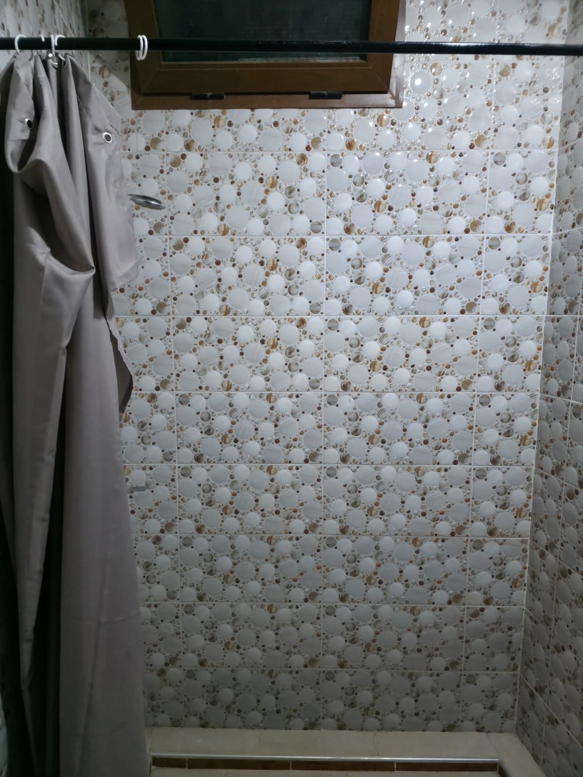 Een badkamer met een betegelde wand met patroon, een douchegordijn en een raam boven de douche.