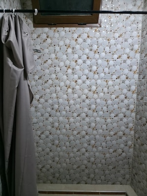 Une salle de bain avec un mur recouvert de carreaux à motifs, un rideau de douche et une fenêtre située au-dessus de la douche.