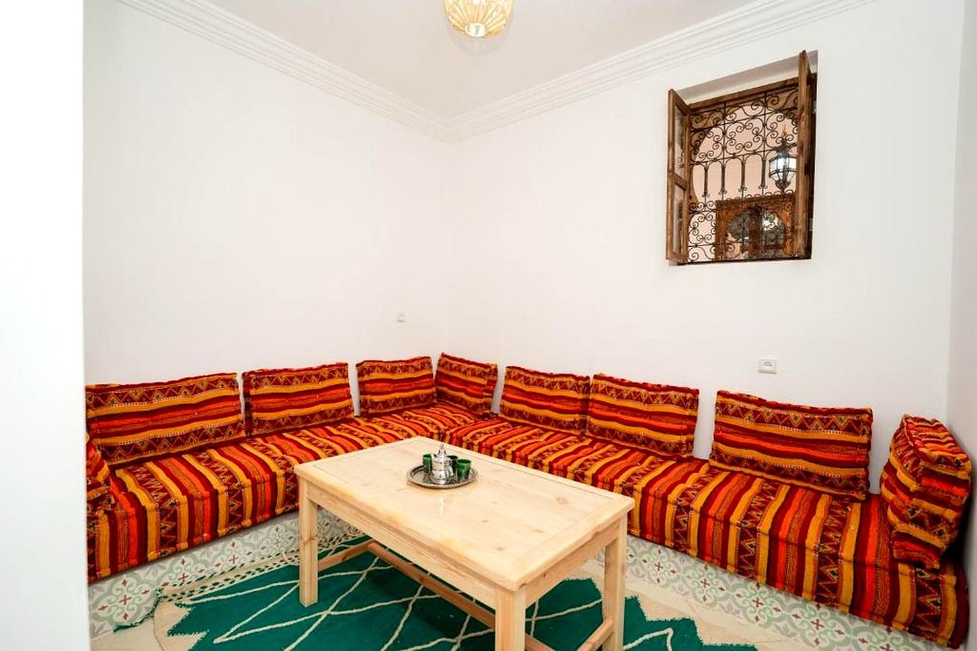 A room with a wooden table and a sofa set with patterned cushions.