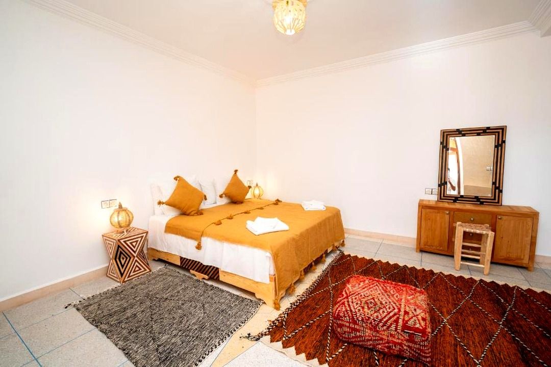 A bedroom with a bed, a nightstand, a dresser, a mirror, and a patterned rug.