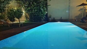 A swimming pool at night with surrounding trees and a building.