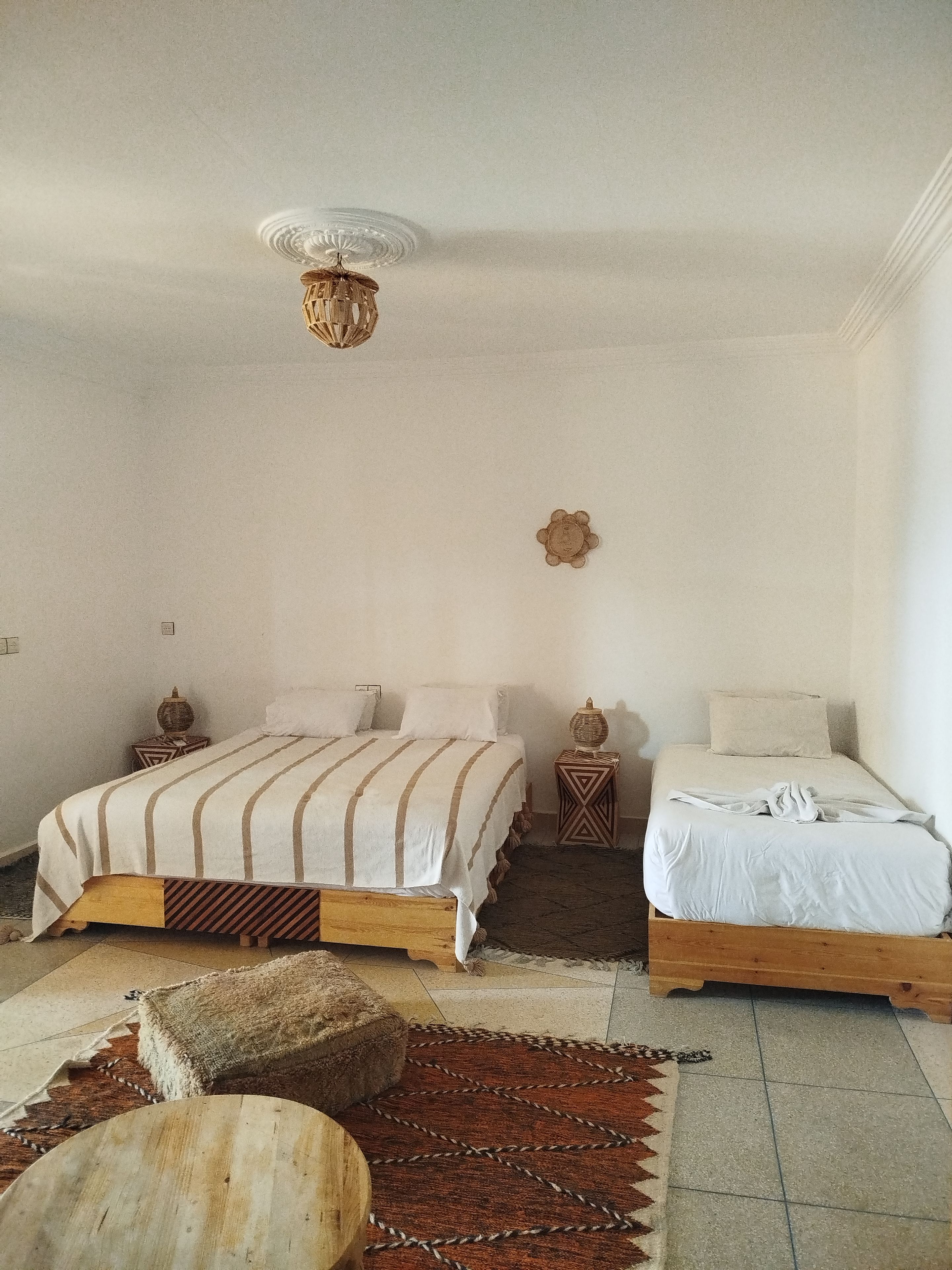A bedroom with two beds, a woven ceiling light fixture, and a patterned rug.