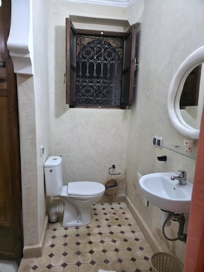 Casa de banho pequena com sanita, lavatório e janela decorativa com grade de metal.