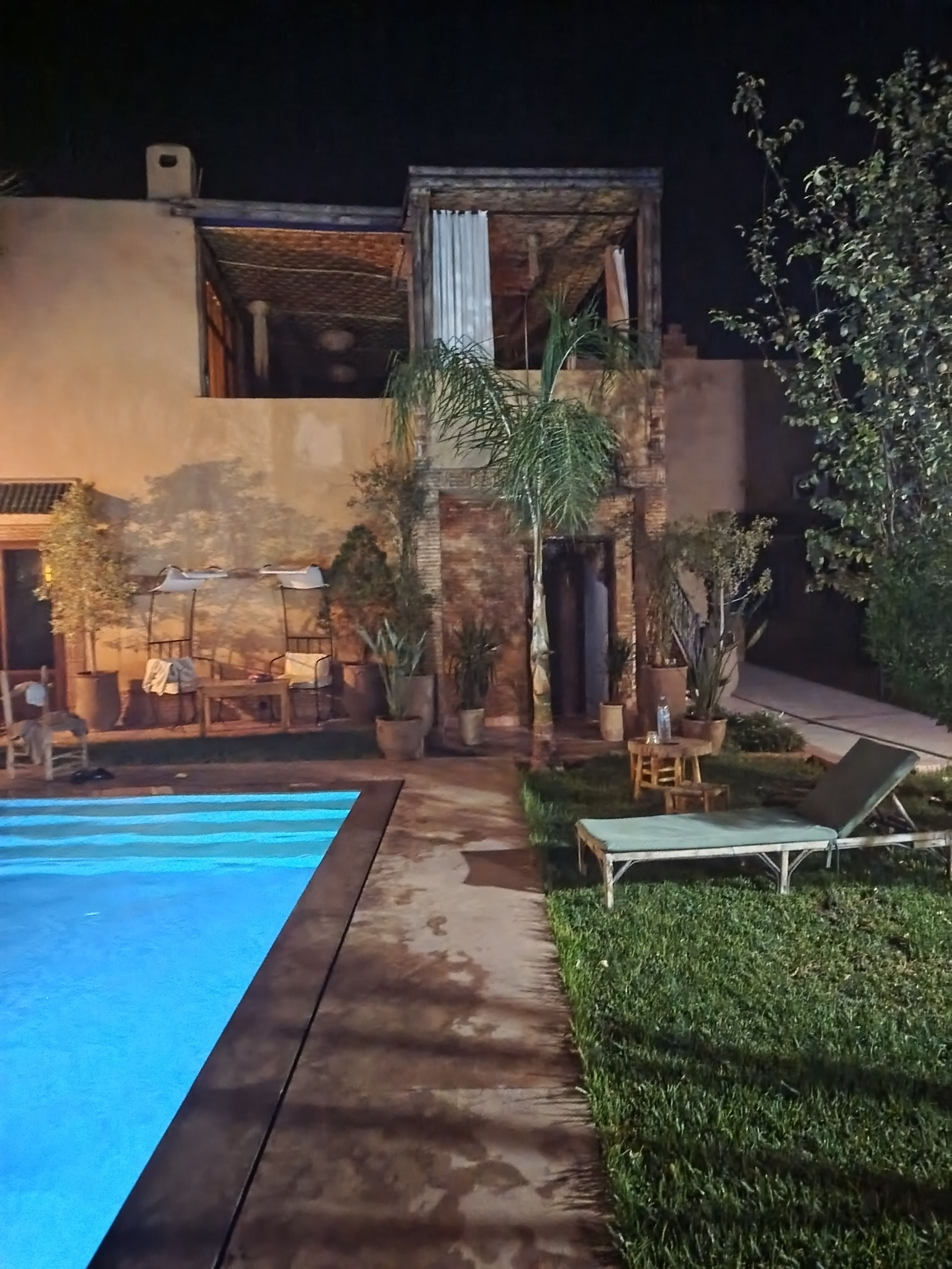 A poolside area with a clear blue pool, surrounded by potted plants and outdoor furniture.