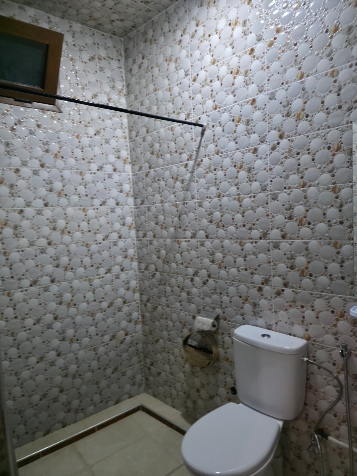 Une salle de bain avec des toilettes, une douche et un mur décoré d’un motif.