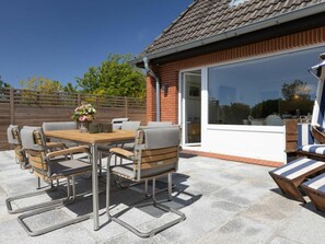 An outdoor patio with a table and chairs, a wooden fence, and a building with a tiled roof. - Holiday Home Heide (Sylt)