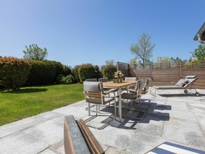 Eine Terrasse im Freien mit Tisch und Stühlen, einem Liegestuhl und einem Holzzaun.
