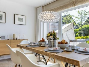 Ein Essbereich mit Holztisch, weißen Stühlen, einer Hängeleuchte und Blick ins Grüne.